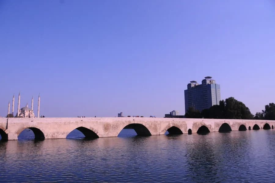 adana'da gezilecek yerler Historic stone bridge and mosque in Adana, Turkey, under clear blue sky.