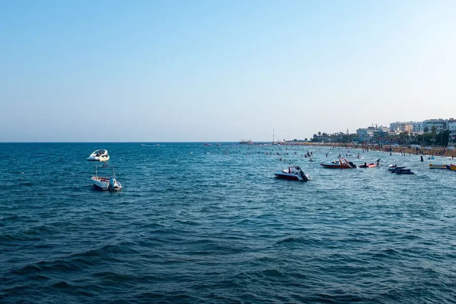 ekimde kıbrısta denize girilir mi A vibrant beach scene with boats and ocean under a clear sky, perfect for summer travel.