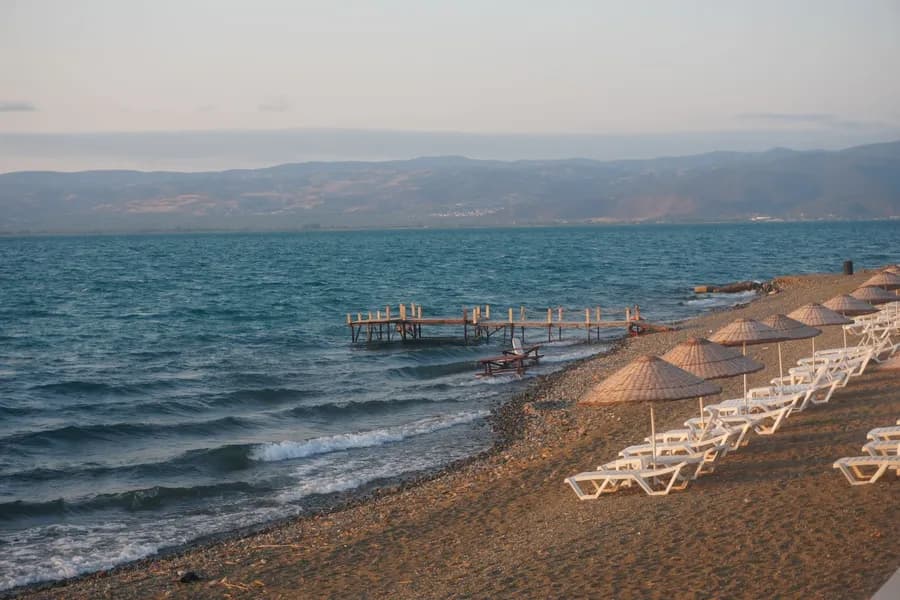 ekimde kıbrısta denize girilir mi Beautiful sunset view of Lake Iznik with empty beach chairs and umbrellas, offering a serene atmosphere.